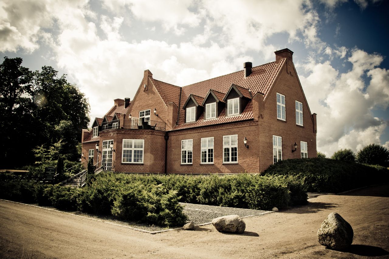 Elegant brick mansion with landscaped garden under a bright sunny sky.