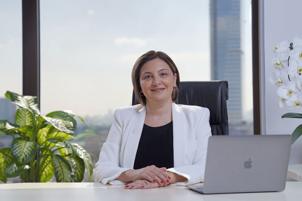 Professional woman in a white suit sitting confidently at a desk with a laptop in a modern office.
